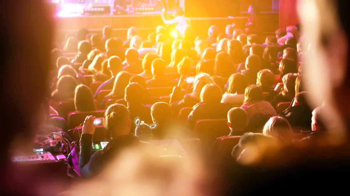 An audience settling into their seats as the house lights dim.