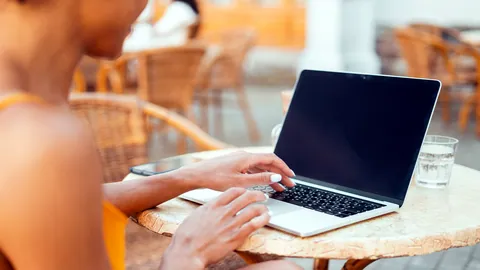 Hands typing on a laptop in a busy morning cafe.