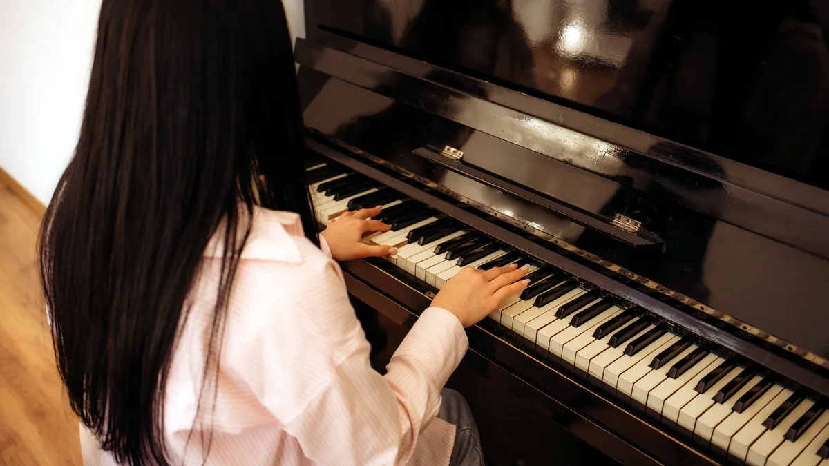 A young musician at an upright piano in a small room.