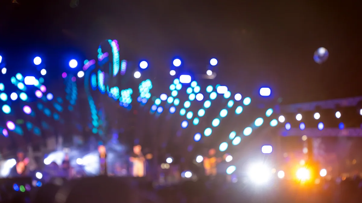 Festival stage lights burning over a gathering crowd at dusk.