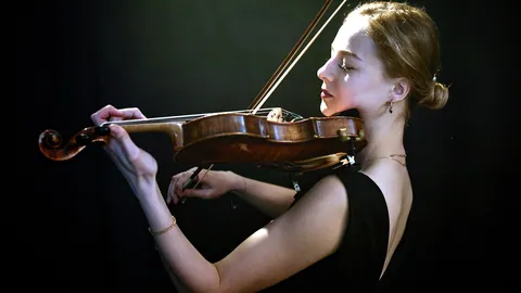 A solo violinist caught mid-bow beneath a single spotlight.