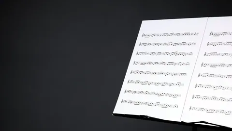 Orchestral sheet music fanned out on a black music stand.
